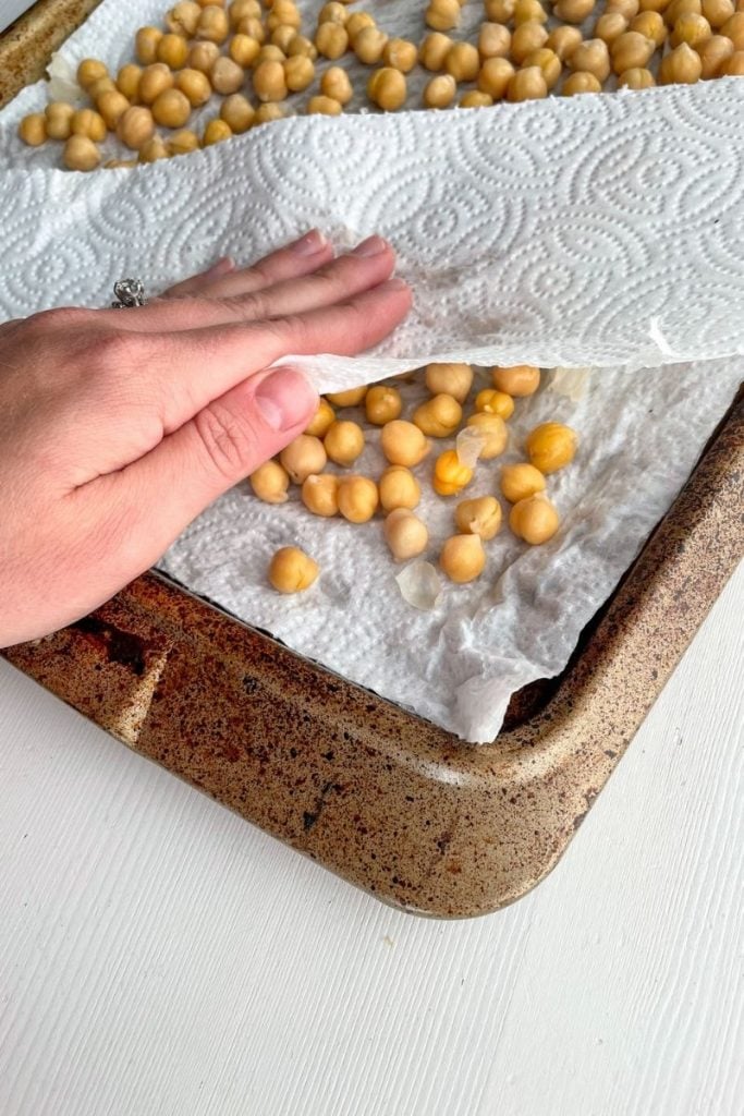 Hand drying off canned chickpeas with paper towel on baking sheet