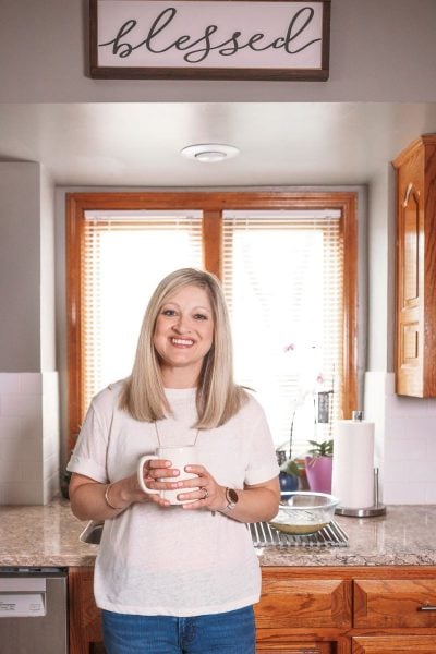 mother holding cup of coffee in kitchen underneath sign that says blessed