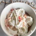 white mug with hot chocolate, whipped cream and chocolate candy sprinkled on top