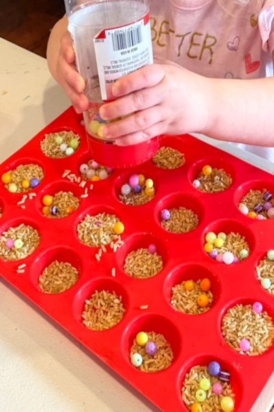 child shaking beads onto rice play muffins