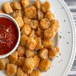 white plate of parmesan air fryer cauliflower gnocchi garnished with parsley and bowl of marinara sauce