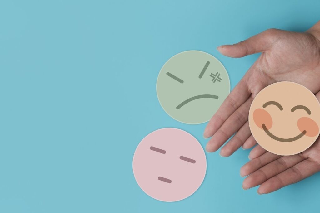 hands layed out on blue background with 3 face cards showing different emotions-- happy, sad, mad