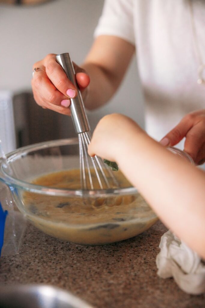 woman's hand whisking bowl of scrambled eggs as toddler hand reaches up