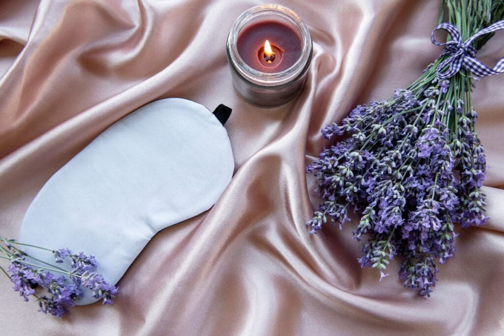 sleep mask and aromatherapy (candle, lavendar) on pink silk sheet to promote better sleep